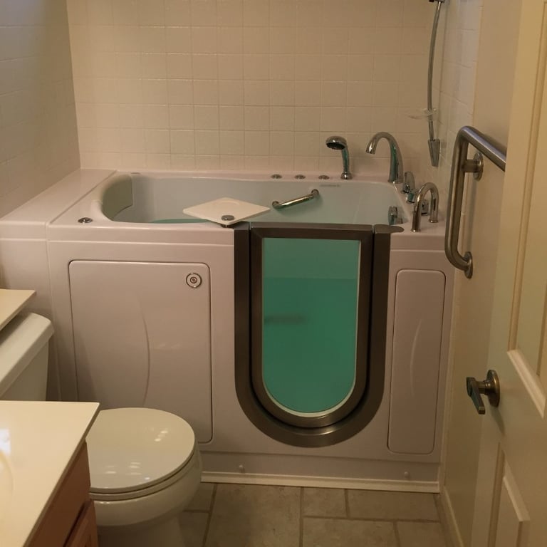 Ella walk-in tub with open inward-swing door, hydrotherapy jets, handheld shower, and stainless steel grab bar installed in small bathroom