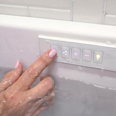 Gros plan d’une main mouillée appuyant sur les boutons du panneau de commande des jets de massage à l’intérieur d’une baignoire à porte Ella