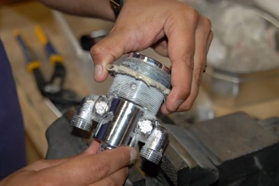 Technician assembling a chrome thermostatic control valve cartridge with pipe fittings on a workshop vise