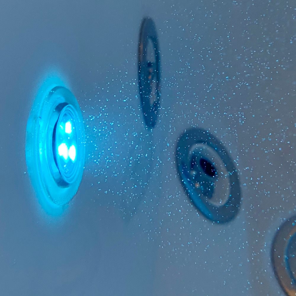 Glowing blue LED chromatherapy light beside the hydro massage jets on the wall of an Ella Royal walk-in tub