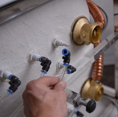 Main d’un technicien raccordant les fixations de tuyauterie de jet d’air sur le panneau intérieur d’une baignoire à porte Ella lors de l’installation