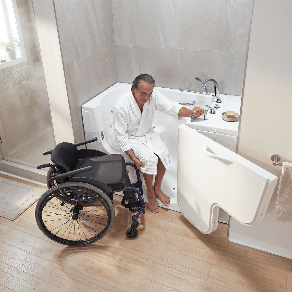 Hombre en bata pasando de una silla de ruedas a la bañera con puerta Ella Transfer26 a través de la puerta en forma de L abierta