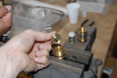 Technician hand-assembling a brass thermostatic control valve cartridge component held over a vise on a workshop bench