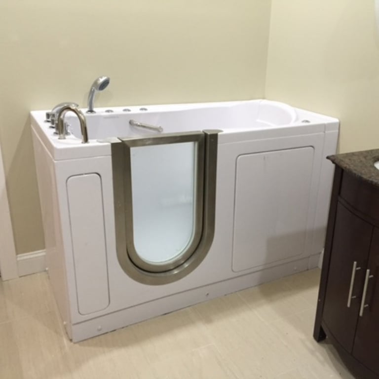 White Ella walk-in tub with stainless steel U-shaped door, handheld showerhead, and hydrotherapy jets installed in a bright bathroom