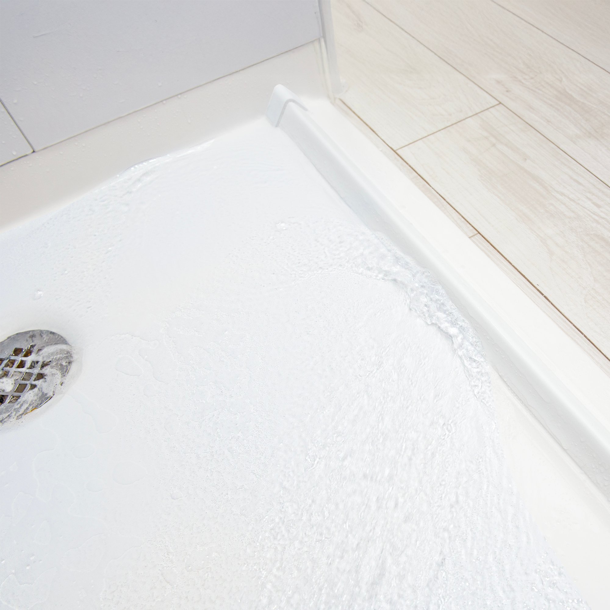 Gros plan sur l'eau s'écoulant sur une base de douche accessible blanche avec un seuil en caoutchouc et un drain chromé