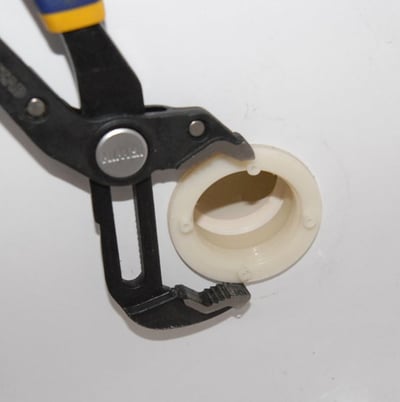 Pince saisissant un raccord de couvercle de retour de vidange en plastique blanc utilisé pour l'installation ou la réparation de la plomberie de baignoire à porte