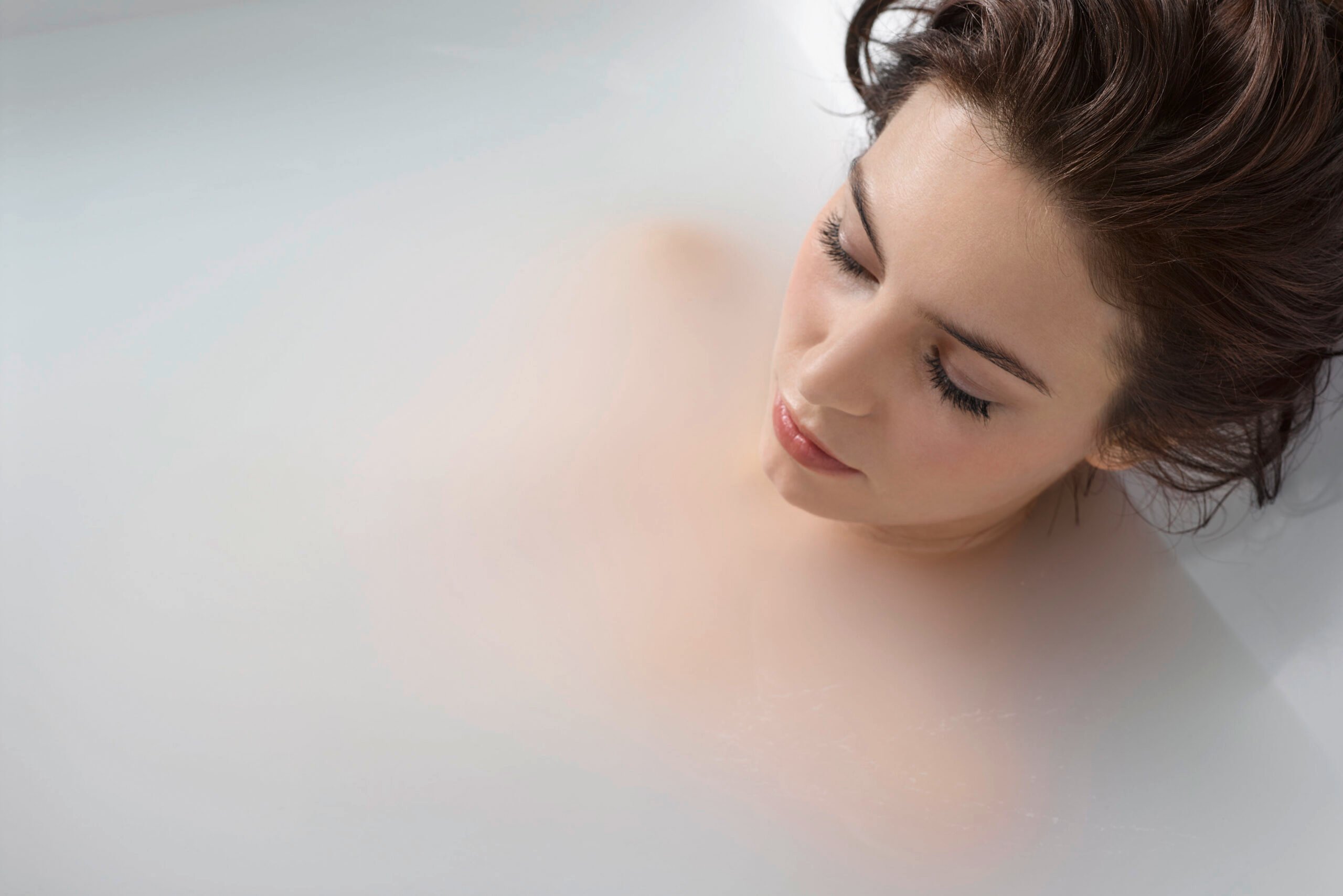 Woman relaxing with eyes closed in an Ella walk-in tub filled with cloudy white hydrogen microbubble water