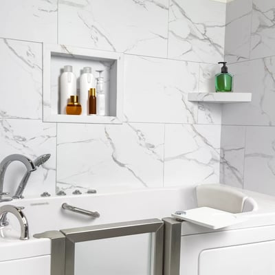 Bañera de hidromasaje Ella con puerta abierta y asiento rodeada de paneles de pared de ducha de mármol Carrara sin lechada con nicho integrado y estante de esquina