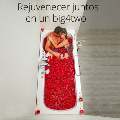 Pareja abrazándose en la bañera de acceso lateral de dos plazas Ella Big4Two llena de pétalos de rosa rojos y rodeada de velas