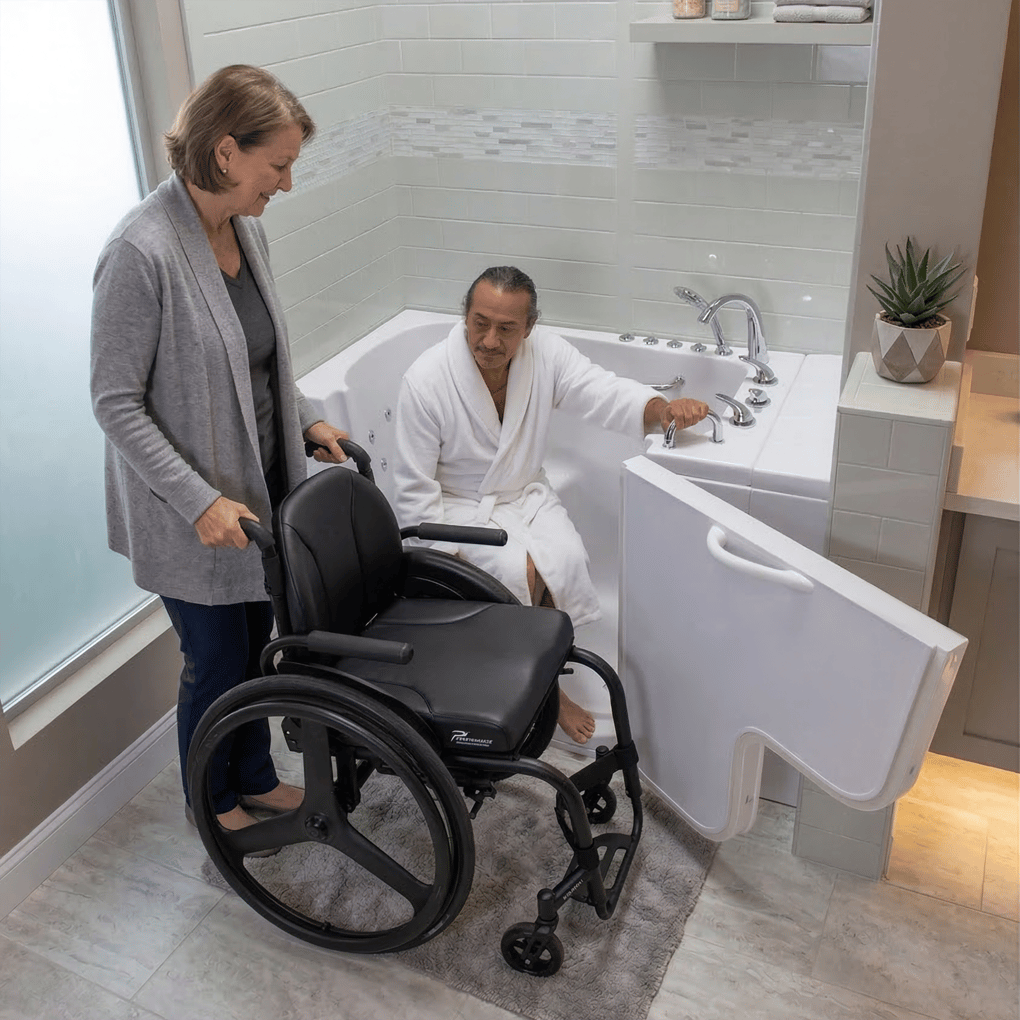 Caregiver assisting a wheelchair user in transferring into the Ella Transfer32 walk-in tub with wide outward swing door
