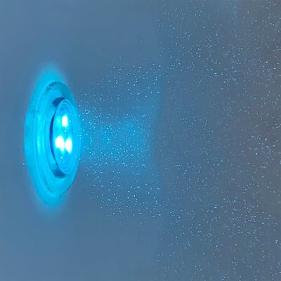 Gros plan d’une lumière de chromothérapie LED bleu lumineux montée dans la paroi d’une baignoire à porte Ella avec gouttelettes d’eau
