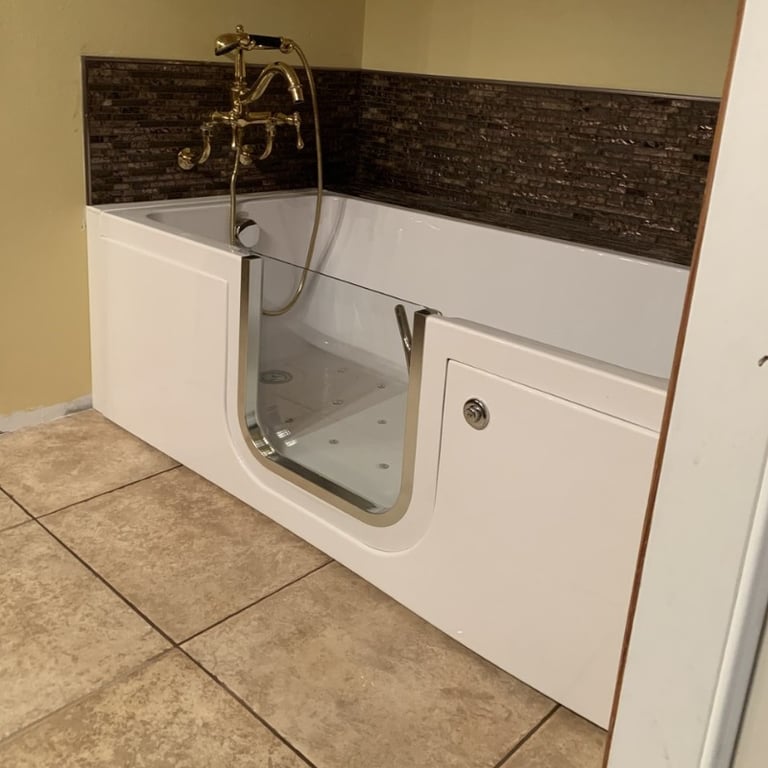 White walk-in tub with open door showing air jets and gold vintage faucet installed against dark mosaic tile backsplash