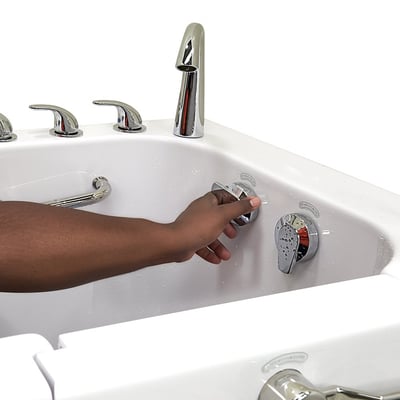 Mano ajustando el mando cromado de control de hidromasaje dentro de la bañera con puerta Ella Big4One con grifería visible