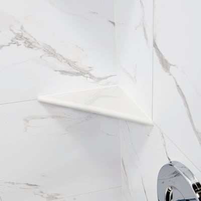 Close-up of a white corner shower shelf mounted on marble-look walls inside an Ella's Bubbles accessible shower stall