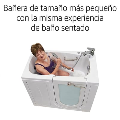 Mujer mayor sentada en la bañera compacta de acceso lateral Ella Mobile usando un rociador de ducha manual con agua de baño de burbujas