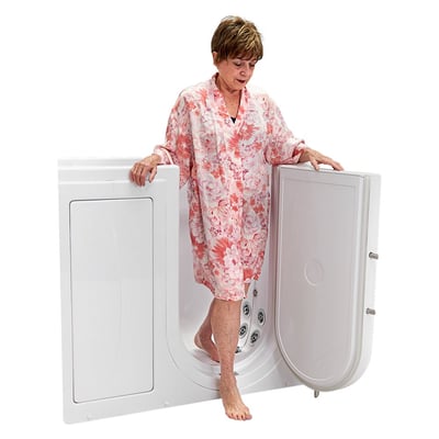 Senior woman in a floral robe stepping out through the open outward swing door of an Ella walk-in tub with jet fixtures visible