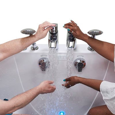 Two people testing flowing water from chrome dual faucets on the Ella Escape two-seat walk-in tub with chromotherapy light