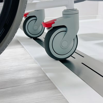 Wheelchair casters rolling over the low threshold of an Ella wheelchair accessible shower base with linear drain