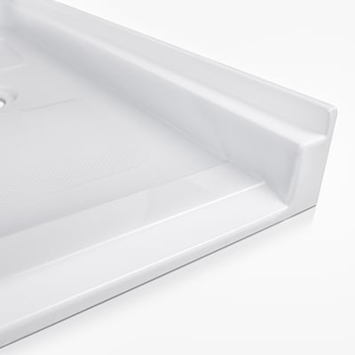 Gros plan du coin du receveur de douche accessible en fauteuil roulant en acrylique Ella montrant le seuil bas et le sol texturé antidérapant