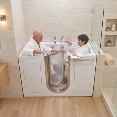 Senior couple in white robes sitting together and smiling inside an Ella companion walk-in tub with two seats and stainless steel door