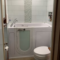 Ella walk-in tub with frosted glass door and chrome grab bar installed in a compact white tiled bathroom
