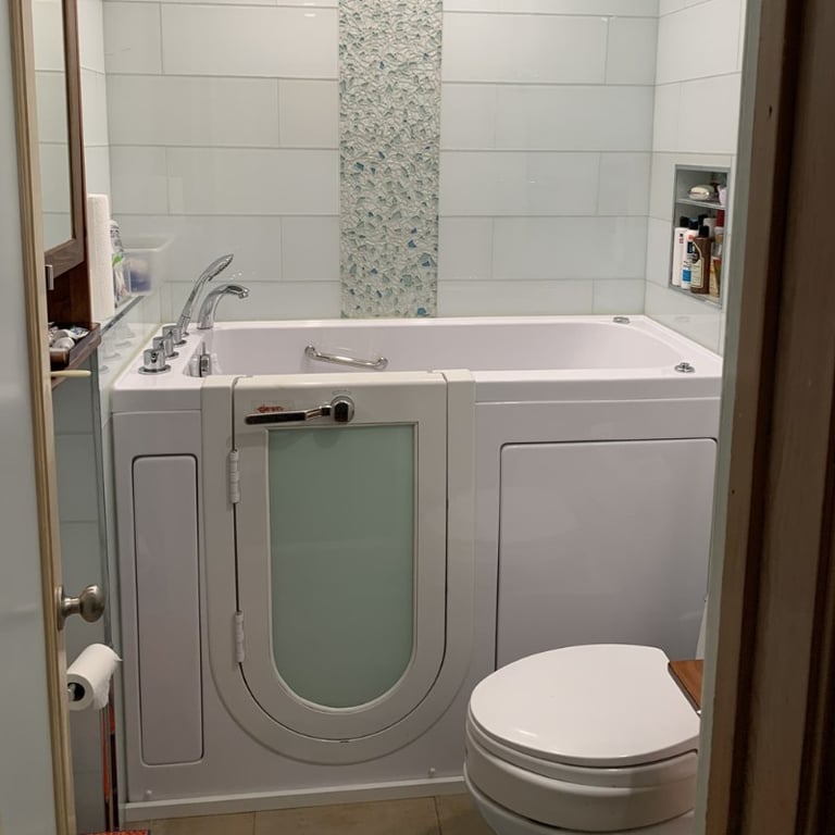 Ella walk-in tub with frosted glass door and chrome grab bar installed in a compact white tiled bathroom