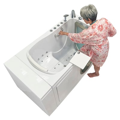Senior woman in a floral dress reaching into the Ella Elite walk-in tub interior with hydro jets, seat, and grab bar visible