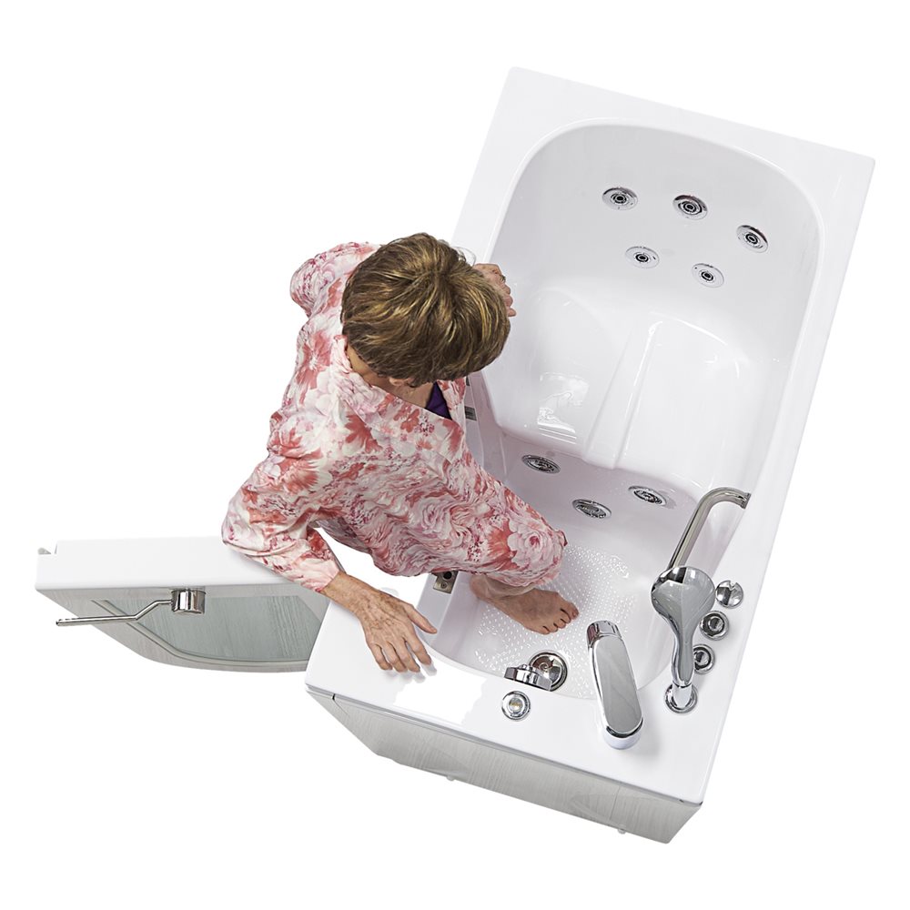 Mujer mayor pasando por encima del umbral bajo para entrar en una bañera con puerta Ella Mobile con la puerta de apertura hacia fuera abierta