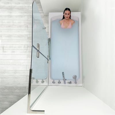 Femme se relaxant les yeux fermés dans une baignoire à porte allongée Ella remplie d’eau, vue de dessus avec porte en verre ouverte