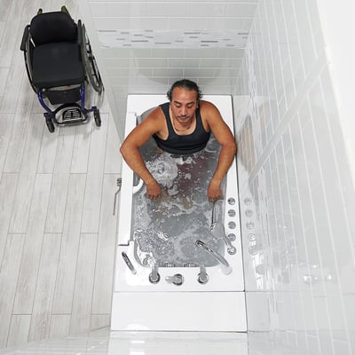 Person soaking in an Ella Transfer30 walk-in tub with hydro massage jets active, mobility aid parked nearby - overhead view
