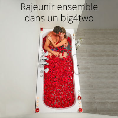 Couple s’embrassant dans la baignoire à porte Ella Big4Two deux places remplie de pétales de roses rouges et entourée de bougies