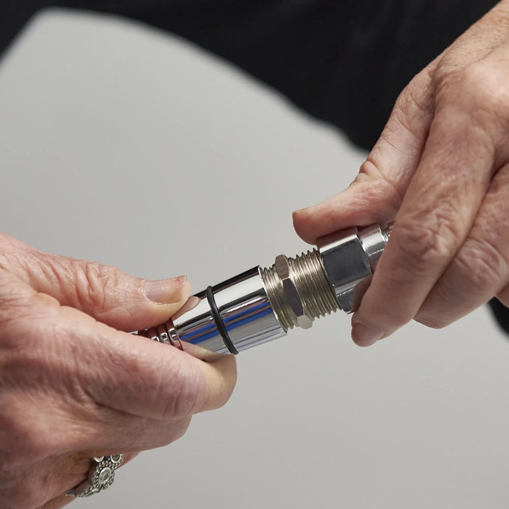 Hands connecting the chrome barrel connector of the leak elimination kit to a walk-in tub hand shower hose