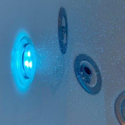 Close-up of glowing blue LED light and water jets on the wall of an Ella Monaco walk-in tub with water droplets