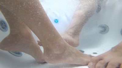 Underwater view of two bathers' feet soaking with hydro jets and blue LED light inside the Ella Big4Two dual walk-in tub