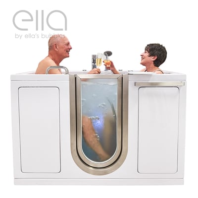 Senior couple smiling and toasting with champagne while soaking in the Ella Companion two-seat walk-in tub with clear door panel