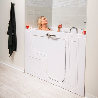 Mujer relajándose con una copa de vino en la bañera accesible para sillas de ruedas Ella TransferXXL con puerta de apertura exterior