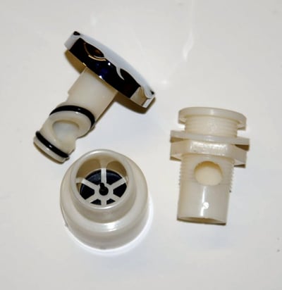 Close-up of three disassembled walk-in tub hydro jet flow rate control components shown on white surface