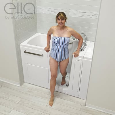 Woman in striped swimsuit stepping out of Ella Ultra Acrylic walk-in tub with open door and grab bars visible