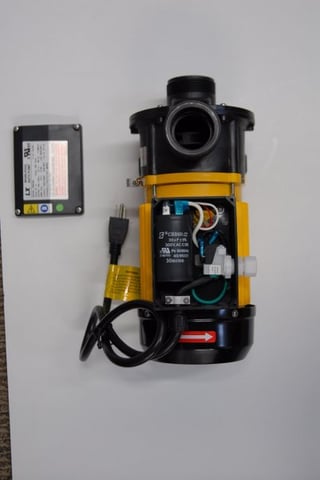 Close-up of an inline water heater assembly unit with yellow and black housing, power cord, and UL certification label