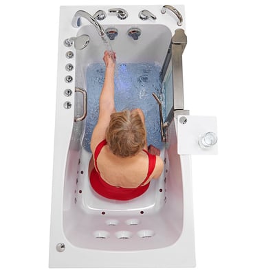 Overhead view of senior woman in red swimsuit reaching toward faucet in Ella Ultimate walk-in tub filling with hydro massage water jets active