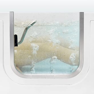 Primer plano a través de la ventana de la puerta de la bañera de acceso mostrando las piernas sumergidas en agua burbujeante de terapia de chorros de masaje de aire.