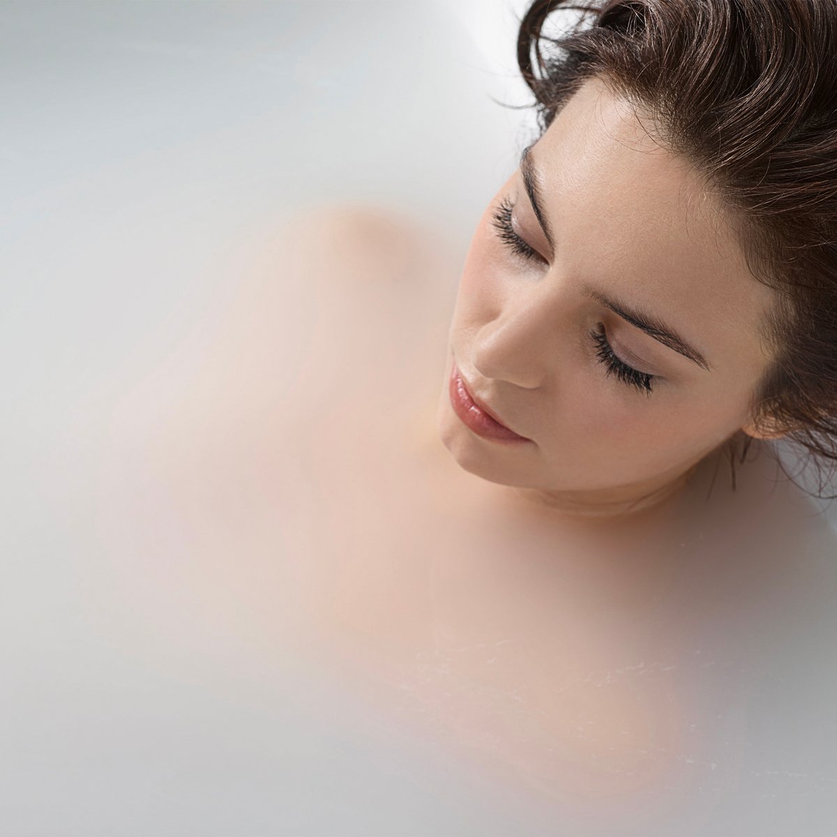 Mujer relajándose en una bañera con puerta Ella llena de agua blanca y lechosa de terapia de microburbujas