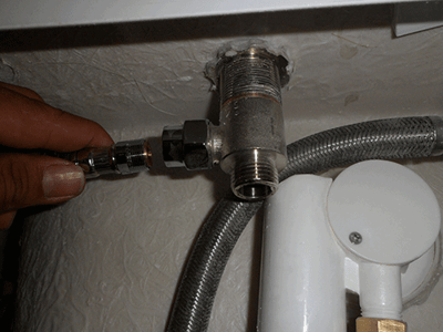Main de l’installateur raccordant un flexible d’alimentation en eau tressé à une vanne d’inverseur chromée lors de l’installation de la plomberie d’une baignoire à porte