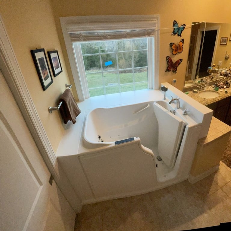 White Ella walk-in tub with open side door installed in a bright bathroom with a garden view window