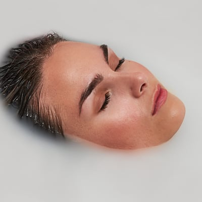 Personne se relaxant les yeux fermés et les cheveux mouillés immergés dans un bain de thérapie par microbulles blanc laiteux dans une baignoire à porte