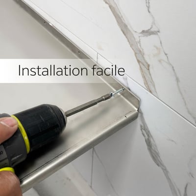 Installateur utilisant une perceuse électrique pour fixer un siège de douche d’angle en acier inoxydable sur des panneaux muraux en marbre