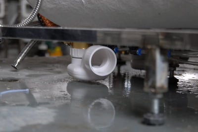 Close-up of a white PVC drain elbow fitting beneath an older discontinued walk-in tub model showing plumbing components