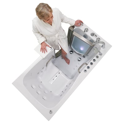 Senior woman in white robe stepping into the Ella Ultimate walk-in tub with open door, anti-slip floor, and hydro jets visible from above