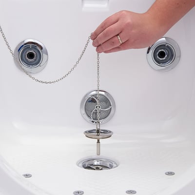 Main soulevant la crépine de vidange chromée par la chaînette à l’intérieur d’une baignoire à porte Ella, montrant un accès facile à la vidange