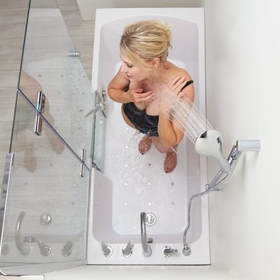 Femme assise dans une baignoire à porte allongée Ella 32x72 utilisant une douchette avec paroi de douche en verre